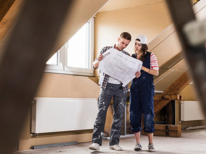 Young couple on construction site of their new home, looking at construction plan